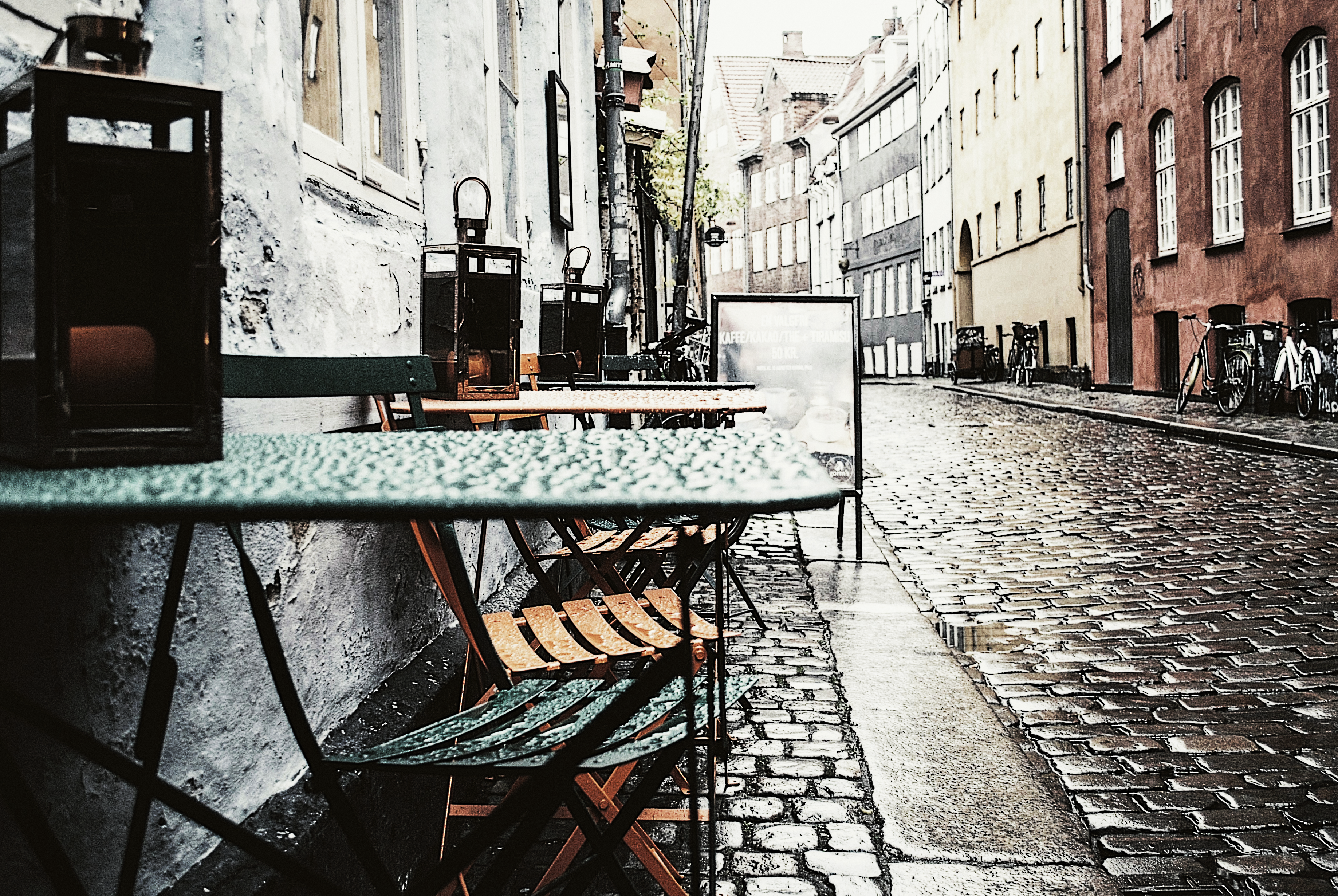 Empty cafe tables and chairs on a wet cobblestone alley